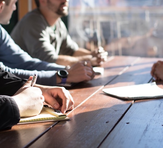 Four people at a work table, they have pads and pens, they seem to be discussing something. 