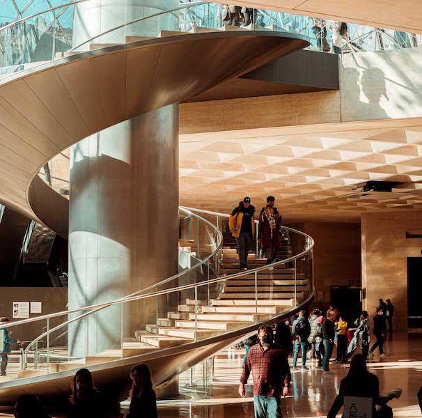 A free-standing spiral staircase in a school building, probably a college. Students wandering around. 